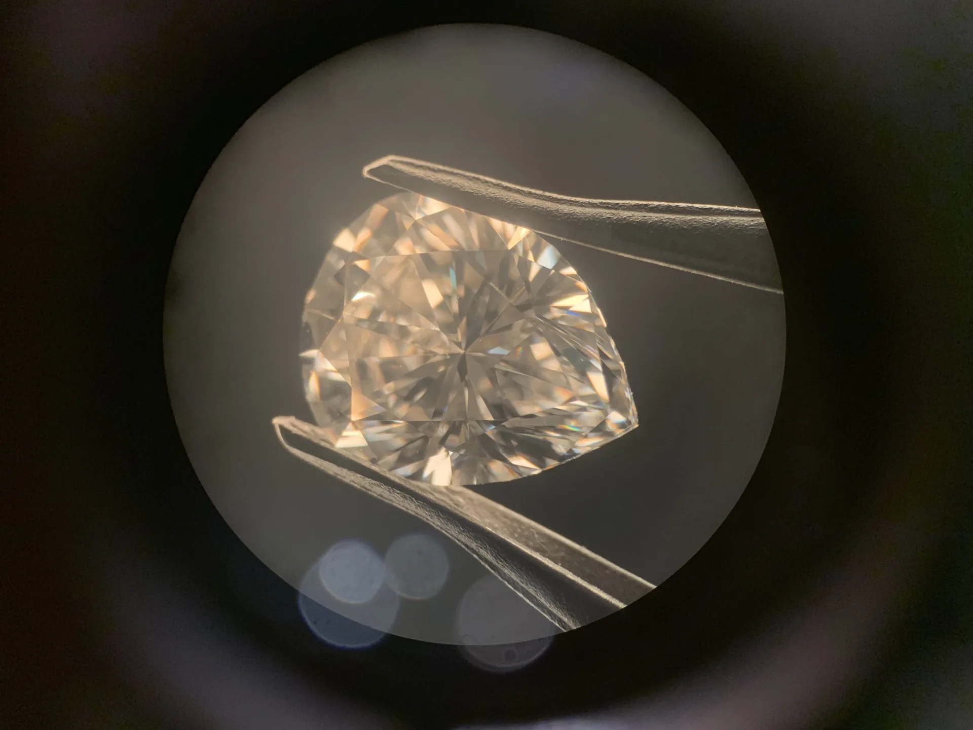 Diamant im Tropfenschliff in der Pinzette, Blick durch das Mikroskopokular, Dunkelfeld